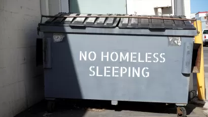 "No homeless sleeping" stenciled on grey dumpster in urban alley