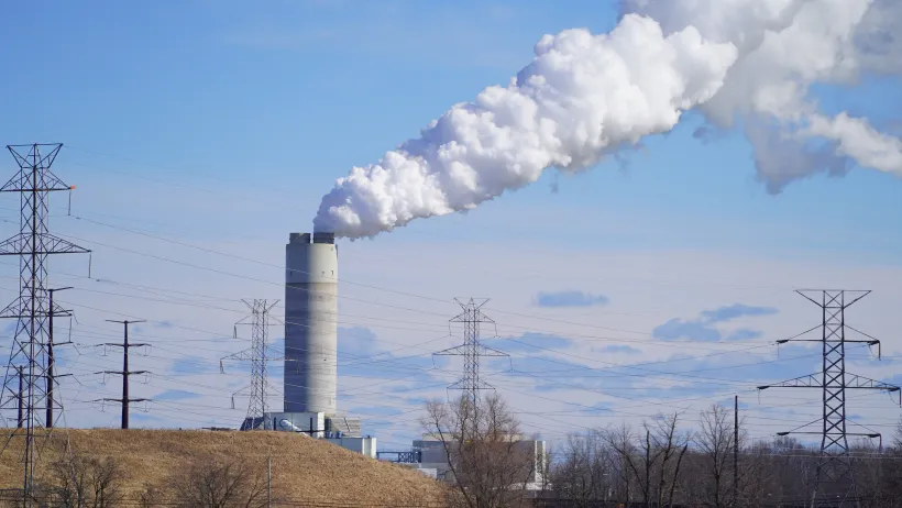 A tall, gray power plant billows smoke into a blue sky.