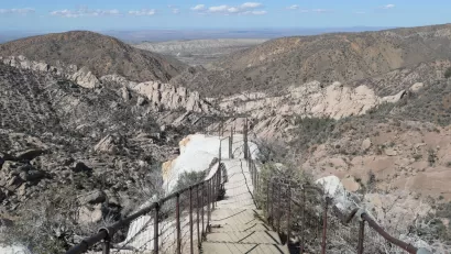 View of hiking trail descending into desert mountains with steps carved into stone and guardrails at Devil's Punchbowl Natural Area, Los Angeles County