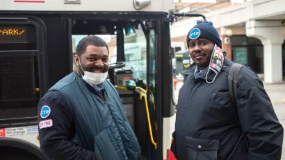 Two Chicago transit operators standing in front of a bus and smiling at the camera