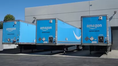 Three blue Amazon delivery trucks at bays at a distribution center