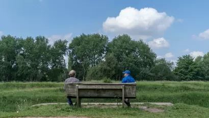 Two friends sit and talk at a social distance in Fletcher Moss park, Manchester, UK