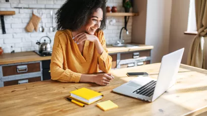 Woman in yellow top sitting at wood kitchen island looking at laptop