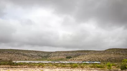 Amtrak Sunset Limited train viewed from the side passing low desert hills in West Texas