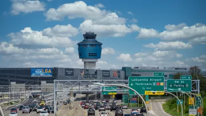 Freeway with traffic leading to LaGuardia Airport with air control tower in the background against white fluffy clouds on bue sky