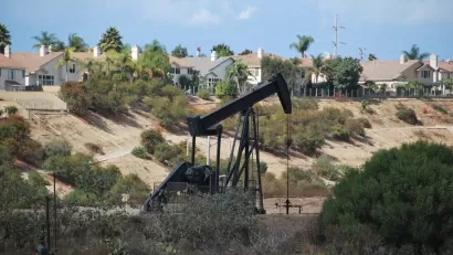 Black pumpjack oil derrick with houses in background