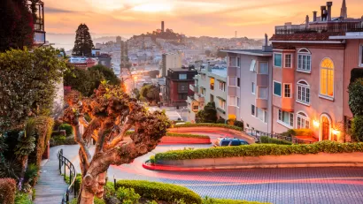 View of downtown San Francisco from top of windy street at sunset with Coit Tower in distance