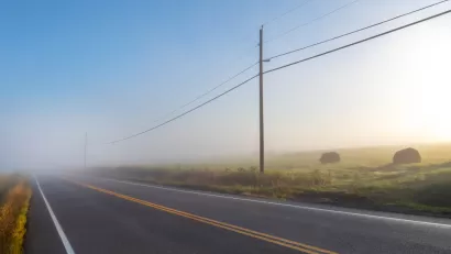 Foggy rural road with power lines and haystacks along the side