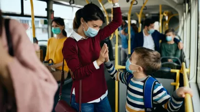 Smiling mother and child on busy public bus wearing Covid-19 protective masks
