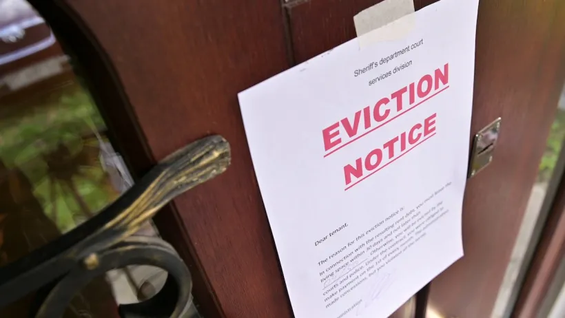 Eviction notice with bold red "Eviction Notice" text taped to brown wooden door.