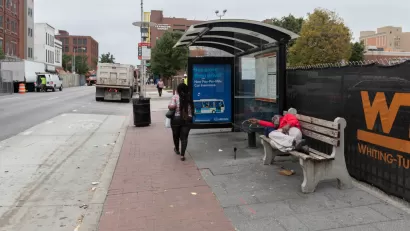 Unhoused person sleeping on bench at bus stop on Baltimore street