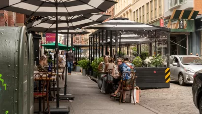 New York City sidewalk with outdoor dining patio with black and white striped umbrellas and black barriers protecting diners from traffic