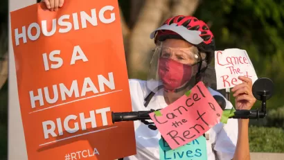 Elderly woman wearing Covid mask holding up "Housing is a human right" sign during tenants' rights protest