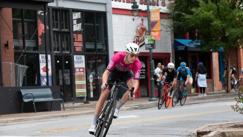 Cyclist in pink jersey and white helmet riding a bike in front of group of several other cyclists in Fayetteville, Arkansas.