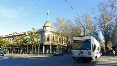 White VTA light rail train passing by historic building in downtown San Jose, California