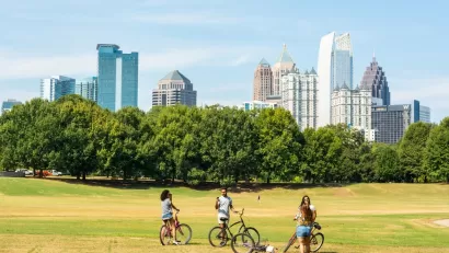 Three people with bikes stopping to chat on grassy field with Atlanta, Georgia skyline in background
