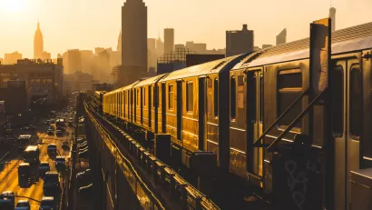 Golden sunset view of New York City subway train on elevated track with Empire State Building in background