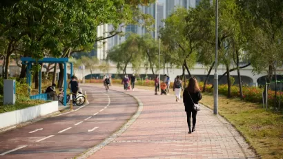 People walking on sidewalk adjacent to bike lane with trees and buildings in background in Hong Kong park