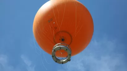 View from below of orange tethered hot-air balloon floating in blue sky