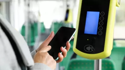 Close-up of person holding up smartphone next to contactless fare reading device on bus