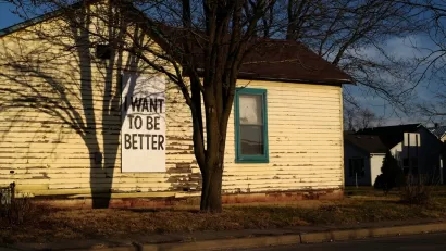 Single-story wooden home with weathered paint and "I want to be better" sign