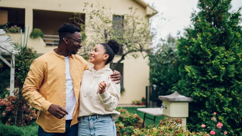 African American couple happily looking at each other in front of a two-story house.