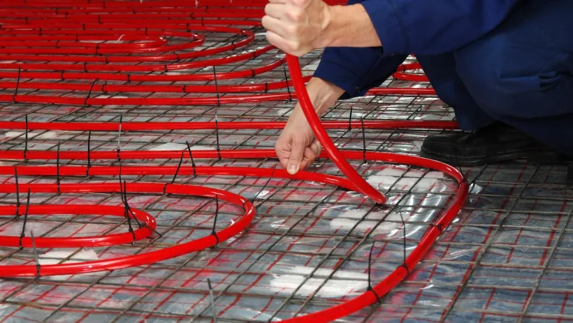 A person lays down red geothermal pipes.