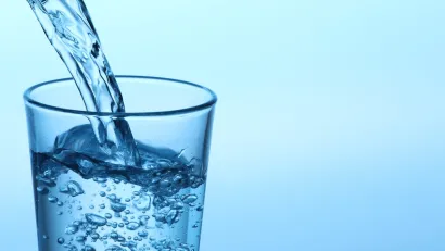 Clear glass with water being poured in against blue background.
