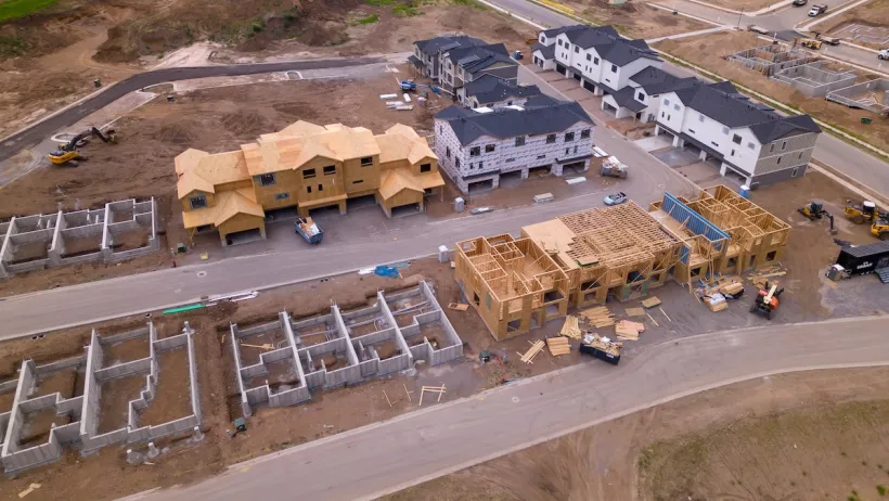 Aerial of wood-framed homes under construction in cleared dirt lots.