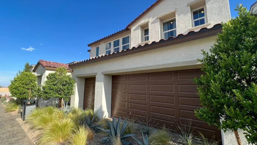Neo-Spanish style new house with brown garage door and xeriscaped small yard.