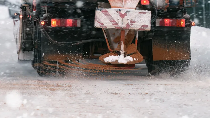 Close-up on back of yellow truck putting down road salt on icy road.