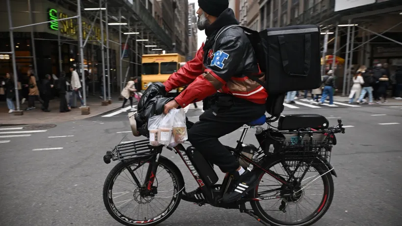 Delivery worker carrying take-out food wearing a black backpack on black bike in New York City.