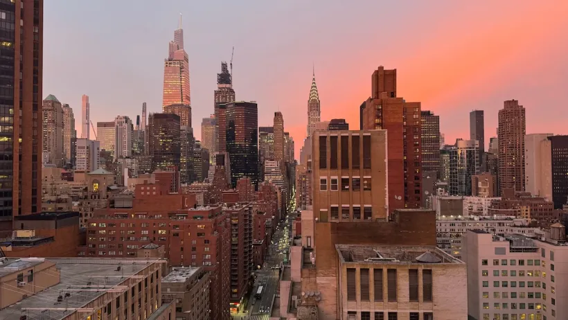 Midtown Manhattan skyline with Chrysler Tower in background against colorful sunset.