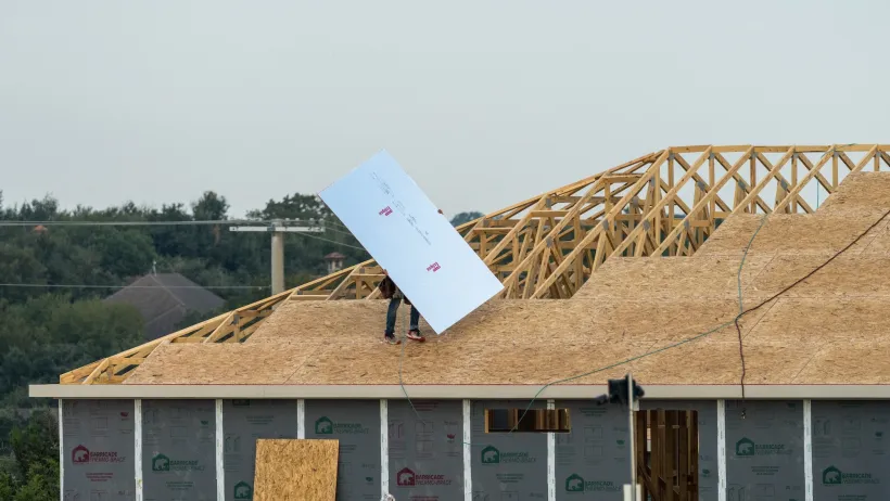 Two workers putting reflective insulation panels into roof of wood-framed house under construction.