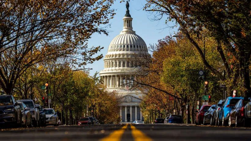 A road, lined with cars, leading to the United States Capital Building.