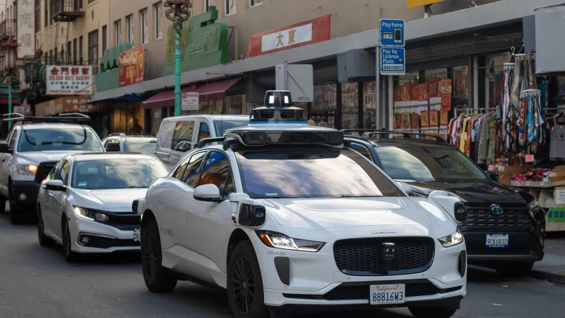 White Waymo self-driving car with camera on top in San Francisco, CA.