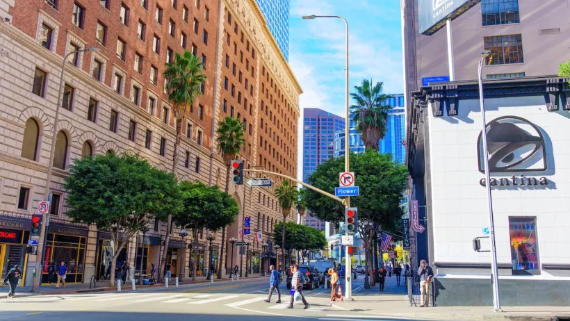 A downtown area in Los Angeles, with a Taco Bell visible. People wait to cross the street towards a tall apartment building.