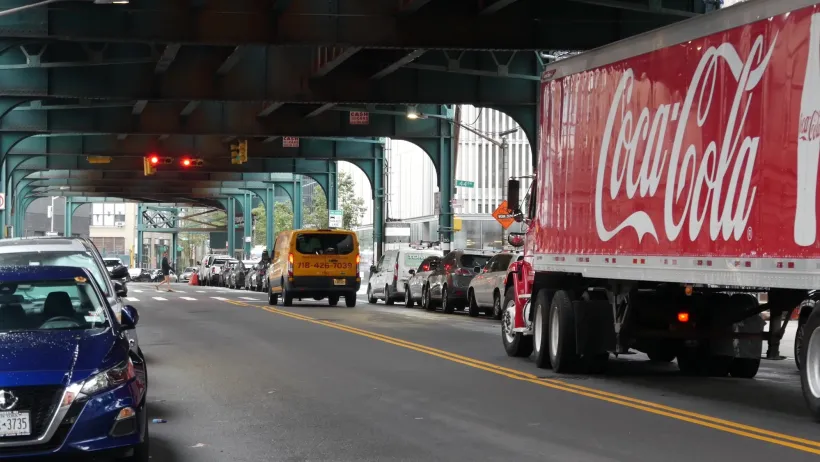 Red Coca Cola truck driving under elevated rail track in New York City.