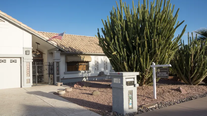 One-story beige home with large cactus in front yard with For Sale sign near sidewalk in Phoenix, Arizona.
