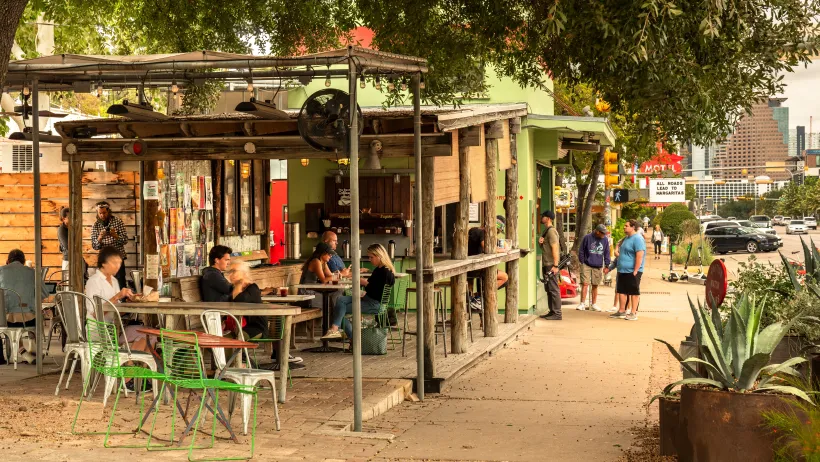 Wooden shops and restaurants in Austin, with people mingling.