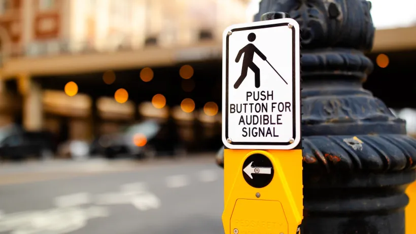 Close-up on pedestrian button with "LOush button for audible signal" below silhouette of person with cane.
