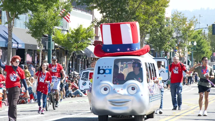 BART train shaped float with face on front and Uncle Sam-style top hat in 4th of July parade.