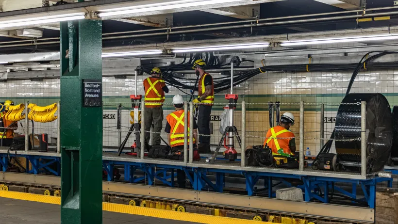 Workers inorange vests working on station infrastructure in New York City subway station.