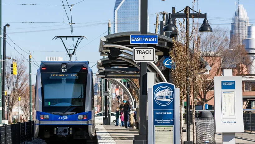A sleek light rail glides through Charlotte, NC, carrying commuters and visitors past busy neighborhoods, skyline views.