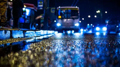 Rainy night in the big city, people standing at the bus stop waiting for the bus. View from the level of asphalt, in blue tones