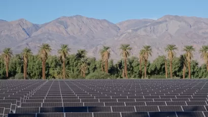 Array of solar panels in the foreground with palm trees and mountains in background, Death Valley, California