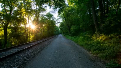 Heritage Rail Trail County Park, York, Pennsylvania with railroad next to unpaved walking/biking trail and sun filtering through green trees