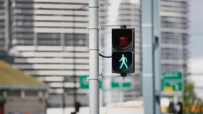 Pedestrian stoplight with green 'walk' silhouette lit up and blurry city buildings in background