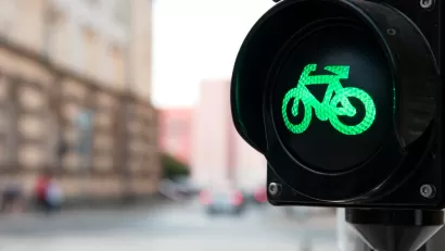 Close-up of black traffic light with green bike symbol lit up and blurry urban scene in background