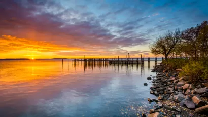Colorful sunset viewed from rockly shoreline on Chesapeake Bay with dock in distance